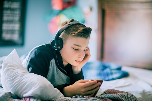 adolescent boy with headphones laying on bed