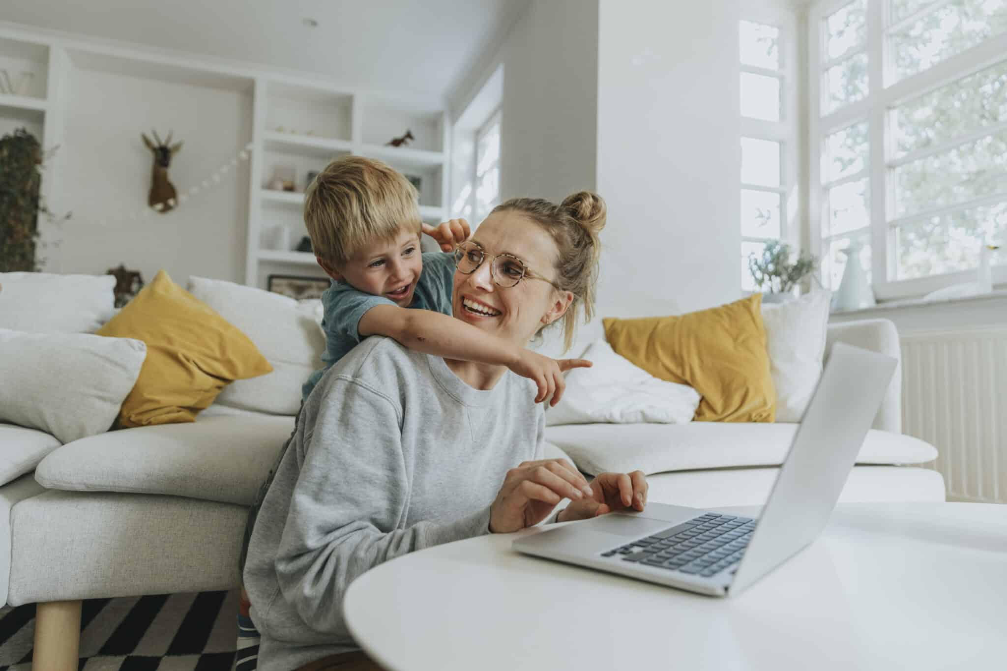 Boy pointing at laptop while standing behind mother