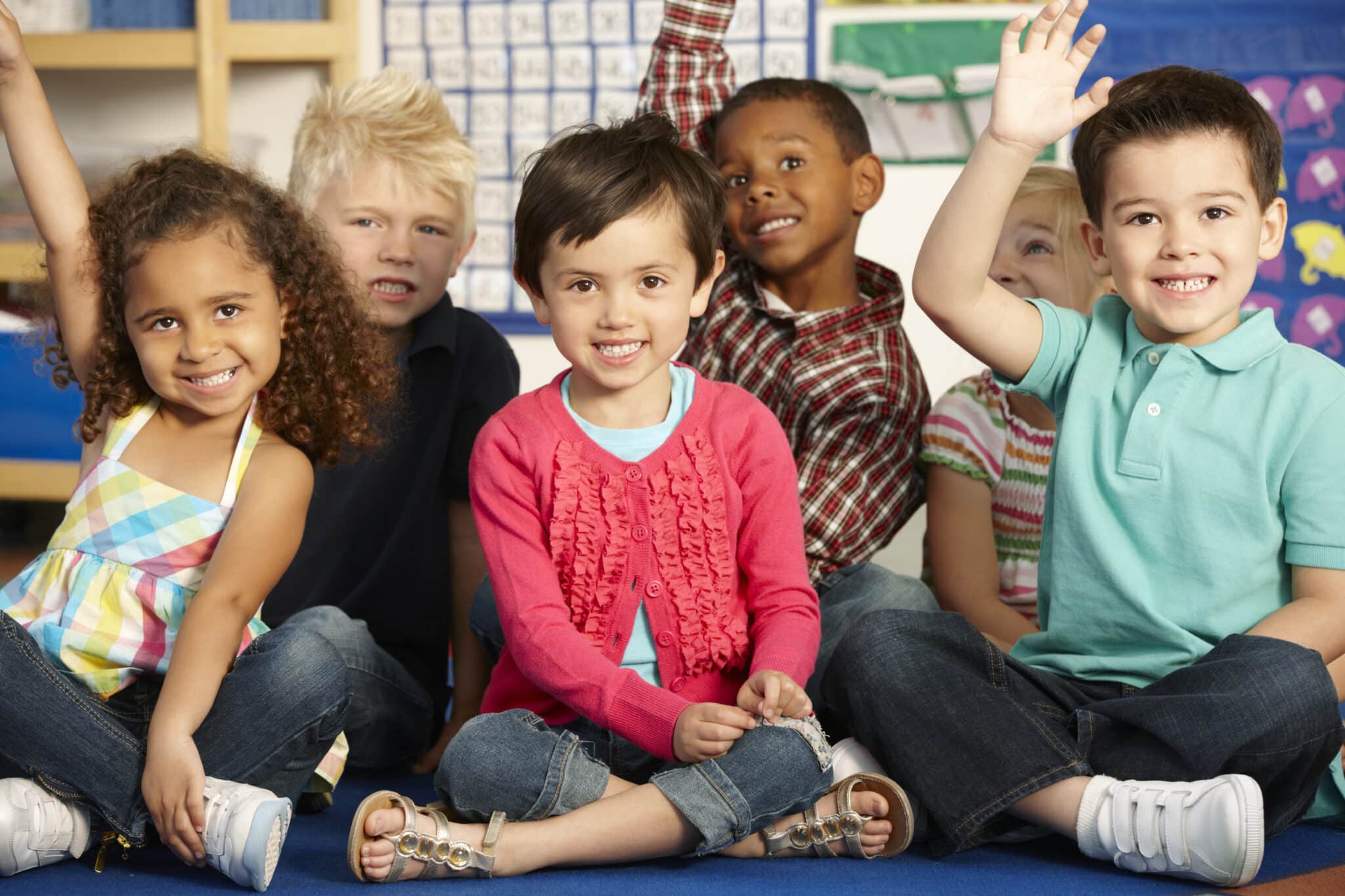 preschool kids raising their hands while sitting on the floor