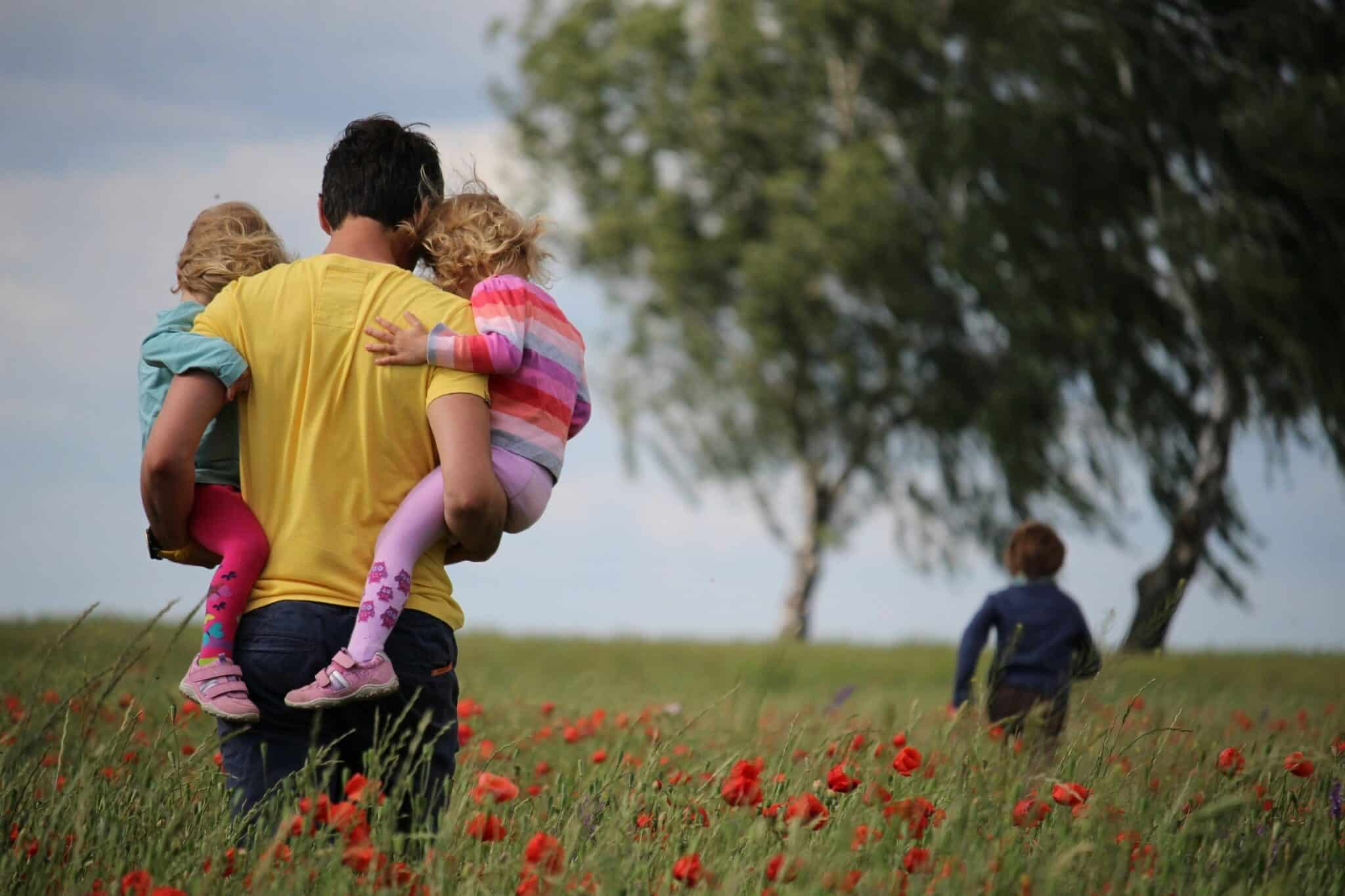 father holding daughters in while walking through field